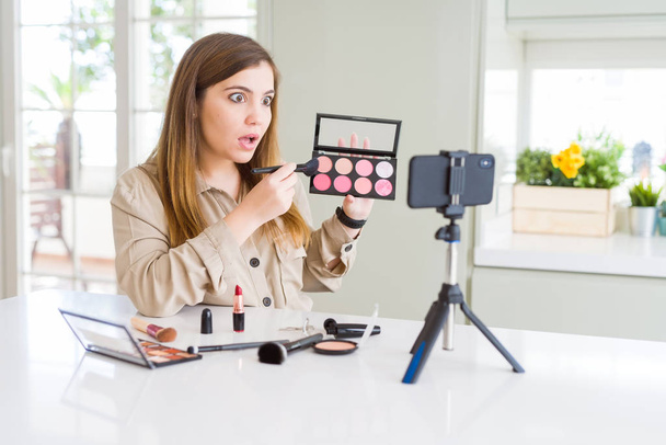 Beautiful young influencer woman recording make up video tutorial scared in shock with a surprise face, afraid and excited with fear expression - Foto, imagen