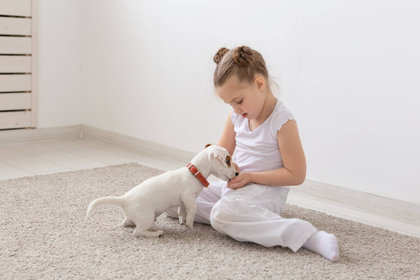 Концепція дітей, домашніх тварин і тварин - дитину Дівчинка в піжамі, граючи з Джек Рассел тер'єр цуценя на підлогу - Фото, зображення