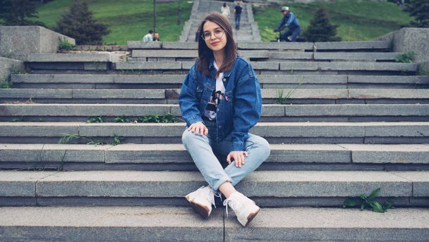 Lifestyle fashion stylish teenager sits on the steps in the city park in denim clothes - Zdjęcie, obraz