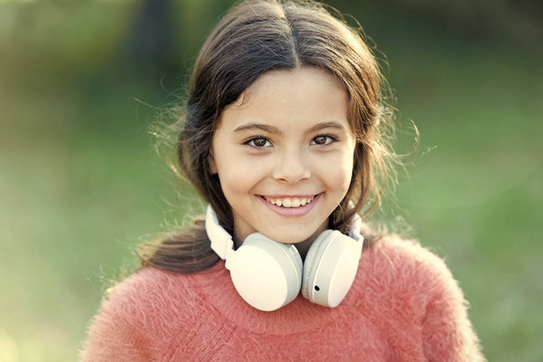 She looks like a music lover. Adorable little girl outdoor. Little girl child wearing headphones. Happy child enjoy listening to music on the go. All she wants to hear is music - Photo, image