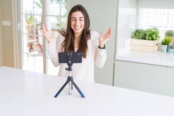 Beautiful young woman recording selfie video with smartphone webcam celebrating mad and crazy for success with arms raised and closed eyes screaming excited. Winner concept - Photo, Image