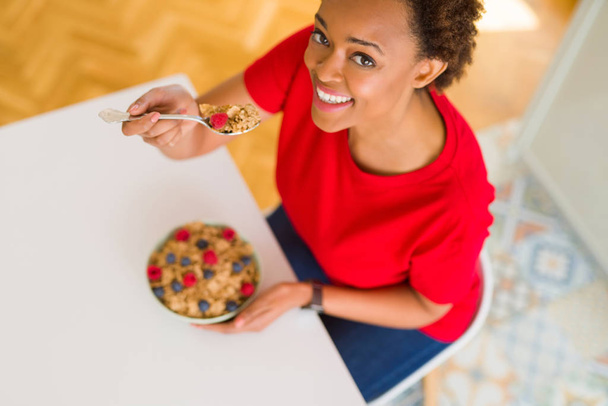 Młode piękne african american kobieta z włosów afro, jedzenie zdrowe płatki zbożowe i owoce jako zdrowe śniadanie - Zdjęcie, obraz