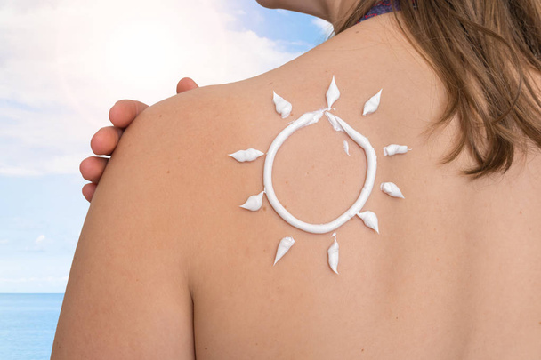 Woman with suntan lotion on her shoulder in sun shape - Фото, изображение