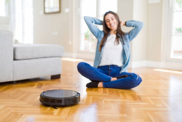 Junge Frau benutzt automatischen Staubsauger, um den Boden zu reinigen und steuert Roboter für die Hausarbeit - Foto, Bild