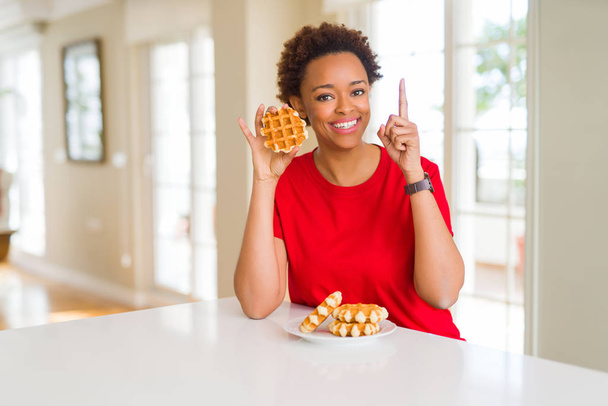 甘いワッフルを食べる若いアフリカ系アメリカ人女性は、幸せな顔で指を指すアイデアや質問に驚きました, ナンバーワン - 写真・画像