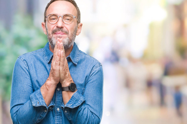 Middle age hoary senior man wearing glasses over isolated background praying with hands together asking for forgiveness smiling confident. - Photo, Image