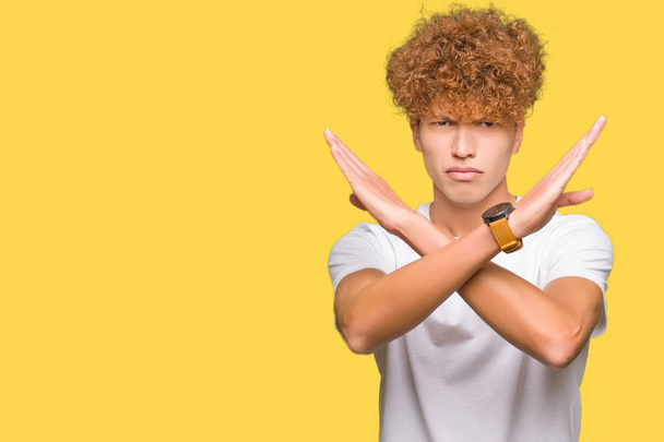 Afro saçlı genç yakışıklı adam rahat beyaz t-shirt giyen Reddi ifade geçen kollar olumsuz işaret yapıyor, kızgın yüz - Fotoğraf, Görsel