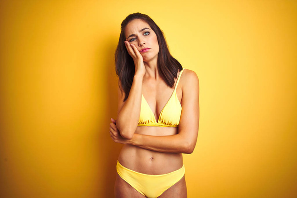 Bella donna che indossa bikini giallo in estate su sfondo giallo isolato pensando cercando stanco e annoiato con problemi di depressione con le braccia incrociate
. - Foto, immagini