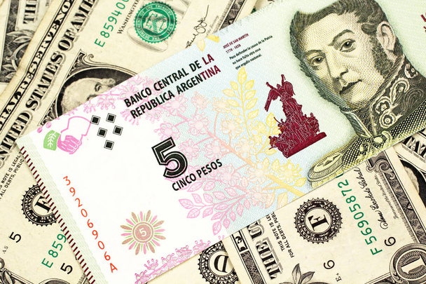 Un billete de banco de cinco pesos de Argentina en un fondo de billetes estadounidenses de un dólar de cerca
 - Foto, Imagen