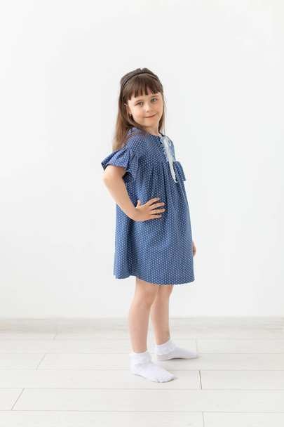 Charming little girl posing in blue polka dot dress on a white background. The concept of classic childrens clothing and stylish children. - Foto, Imagem