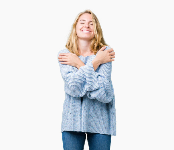 Красивая молодая женщина в голубом свитере на изолированном фоне обнимает себя счастливой и позитивной, уверенно улыбаясь. Самолюбие и забота о себе
 - Фото, изображение