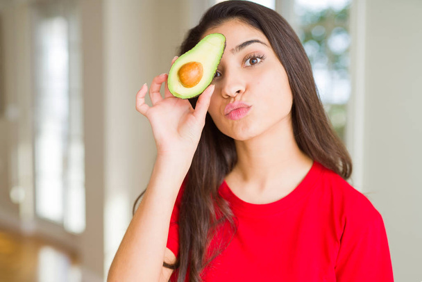 Beautiful young woman holding healthy avocado sending a kiss - Photo, Image