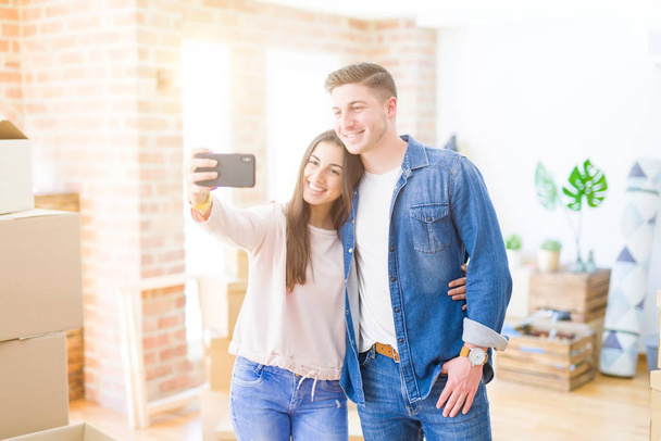 美しい若いカップルは、スマートフォンで自分撮り写真を撮って幸せに微笑み、新しい家に引っ越して非常に興奮 - 写真・画像
