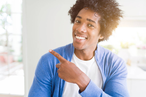 Afrikalı-Amerikalı adam neşeli bir gülümseme ile el ve parmak kadar yan yüzünde mutlu ve doğal ifade ile işaret yüz ile evde - Fotoğraf, Görsel