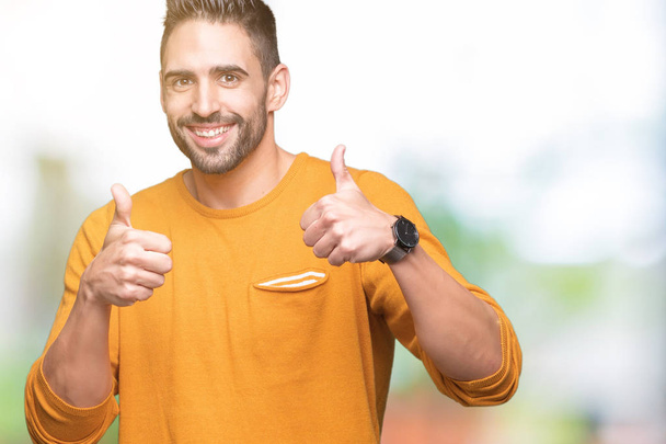 Young handsome man over isolated background success sign doing positive gesture with hand, thumbs up smiling and happy. Looking at the camera with cheerful expression, winner gesture. - Photo, Image