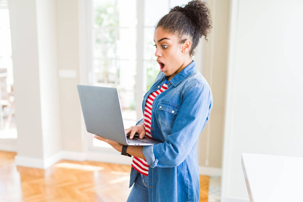 Fiatal afro-amerikai lány áll dolgozik a laptop ijedt a sokk egy meglepetés arc, fél, és izgatott a félelem kifejezés - Fotó, kép