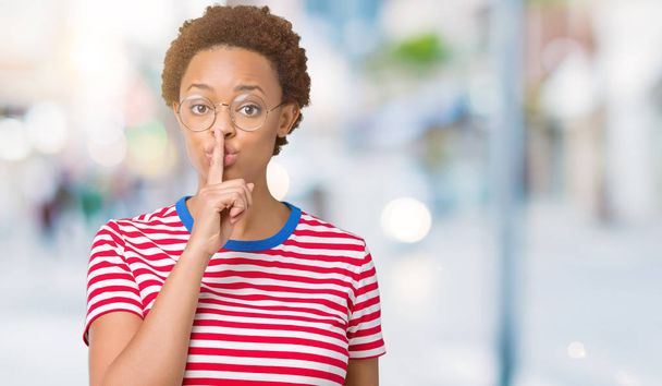 Linda jovem afro-americana usando óculos sobre fundo isolado pedindo para ficar quieta com o dedo nos lábios. Silêncio e conceito secreto
. - Foto, Imagem