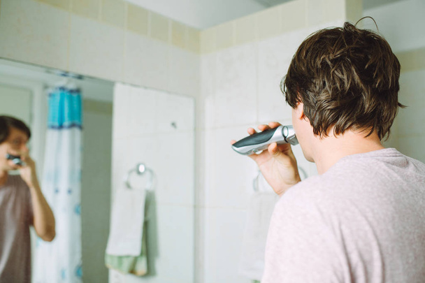 Молодой человек бритьё лицо usung электрическая бритва в ванной комнате
 - Фото, изображение
