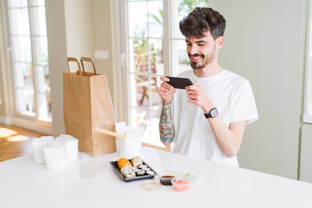 Young man taking pictures with smartphone of sushi asian food from take away delivery - Photo, Image