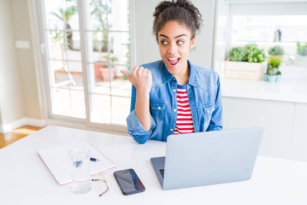 Joven afroamericana estudiante mujer usando computadora portátil señalando y mostrando con el pulgar hacia arriba a un lado con la cara feliz sonriendo
 - Foto, Imagen