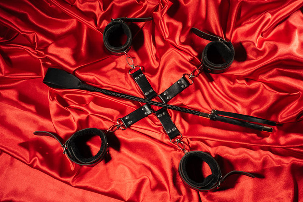 Top view of bdsm outfit. Bondage and spank on the red linen. Adult sex games. Kinky lifestyle. - Fotografie, Obrázek