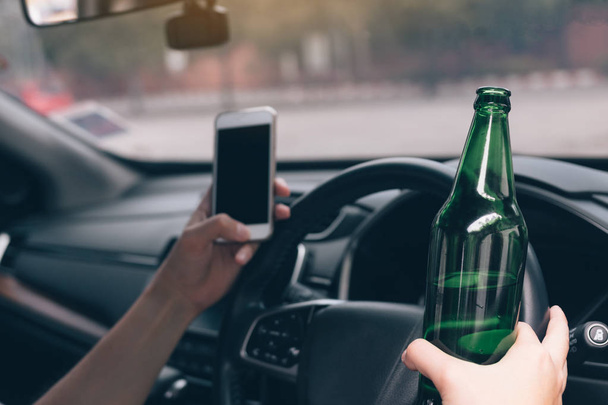 アジア人の男性が車の中の携帯電話を使用してアルコールを飲む - 写真・画像