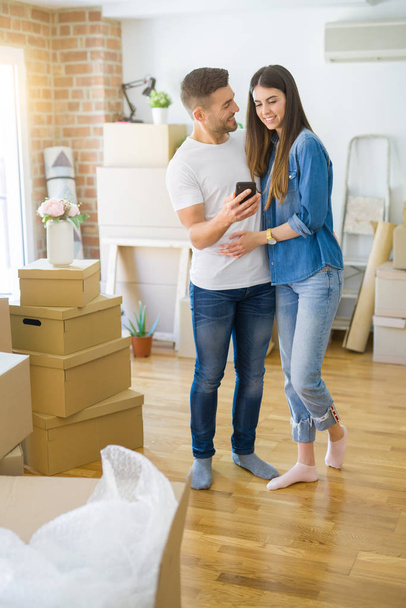 新しい家に引っ越す若いカップルは、新しいアパートのために非常に幸せに微笑むスマートフォンを使用して - 写真・画像