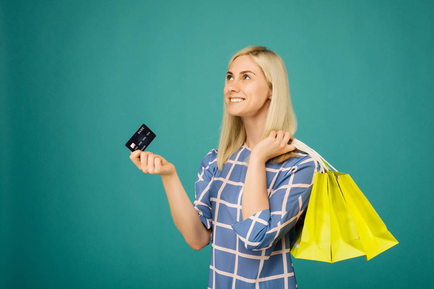 glückliches Mädchen in karierter Bluse hält Kreditkarte und Einkaufstasche in der Hand - Foto, Bild