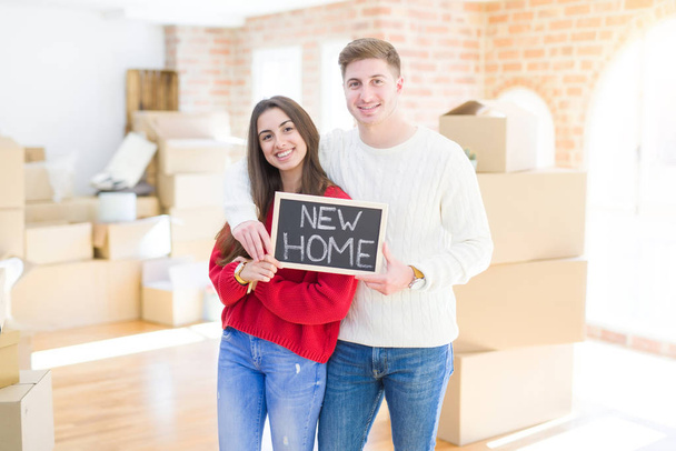 Όμορφο νεαρό ζευγάρι αγκαλιάζει την αγάπη και κρατώντας μαυροπίνακα μετακίνηση σε ένα νέο σπίτι, χαμογελαστός χαρούμενος για το νέο διαμέρισμα - Φωτογραφία, εικόνα