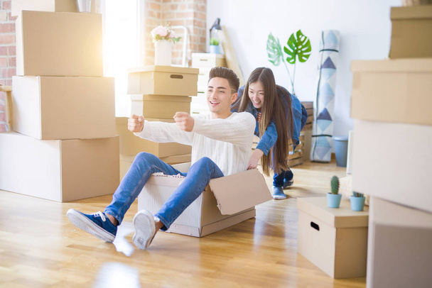 Funny asian couple having fun, riding inside cardboard box smiling happy, very excited moving to a new house - Foto, Imagen