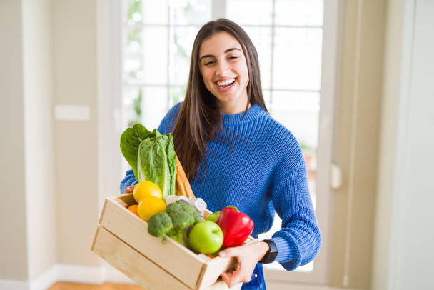 Молодая женщина улыбается, держа деревянную коробку с продуктами от родов
 - Фото, изображение