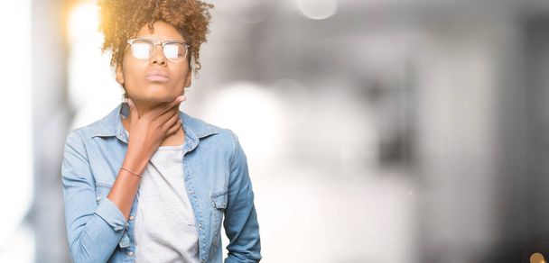 Красивая молодая африканская американка в очках на изолированном фоне трогает болезненную шею, болит горло от гриппа, заноз и инфекция
 - Фото, изображение