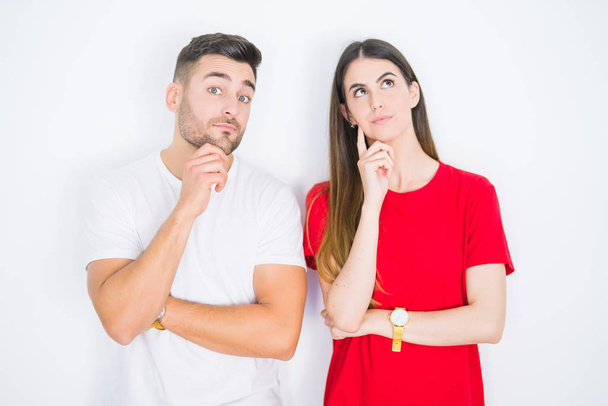 Young beautiful couple together over white isolated background with hand on chin thinking about question, pensive expression. Smiling with thoughtful face. Doubt concept. - Photo, Image