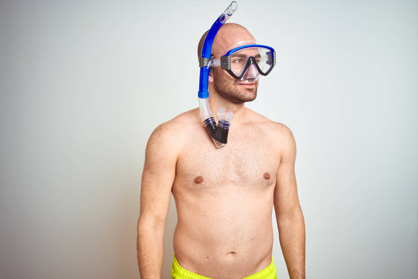 Young man wearing diving snorkel goggles equipent over isolated background looking away to side with smile on face, natural expression. Laughing confident. - Photo, Image
