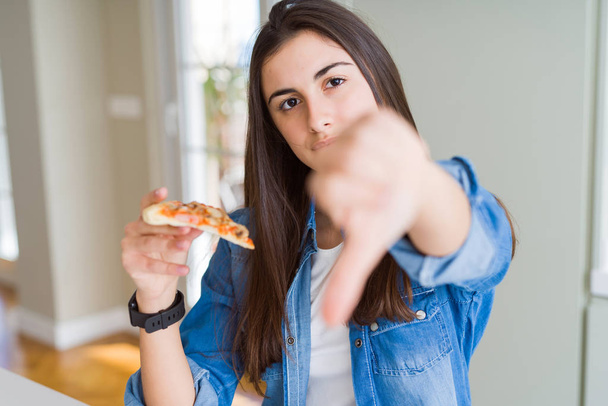Красива молода жінка їсть шматочок смачної піци з розлюченим обличчям, негативний знак, що показує нелюбов до великих пальців вниз, концепція відторгнення
 - Фото, зображення