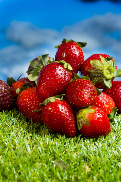 Red strawberries in a wooden plate on green grass with blue sky  - Foto, Imagem