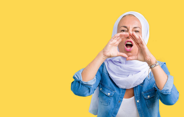 Восточная арабская женщина средних лет носит арабский хиджаб на изолированном фоне, крича сердито, с руками над ртом.
 - Фото, изображение