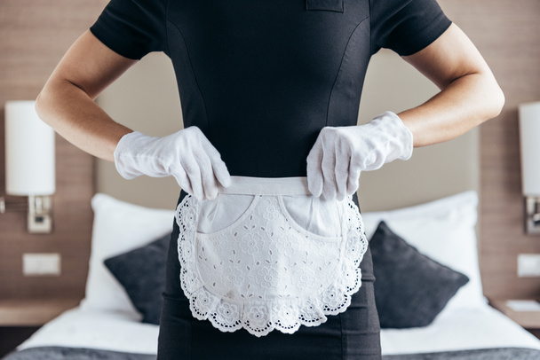 partial view of maid in white gloves and apron in hotel room - Fotoğraf, Görsel