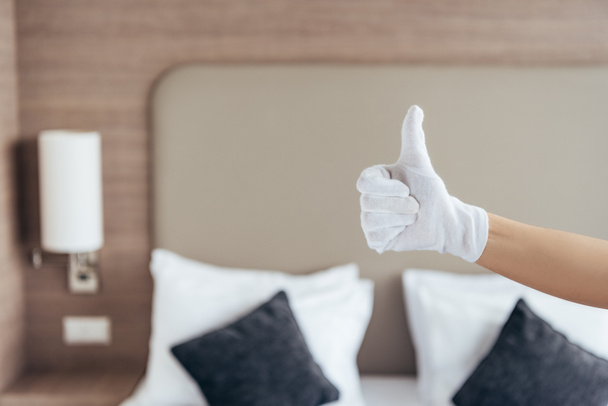 μερική θέα της καμαριέρας σε λευκό γάντι δείχνοντας αντίχειρας στο δωμάτιο του ξενοδοχείου - Φωτογραφία, εικόνα