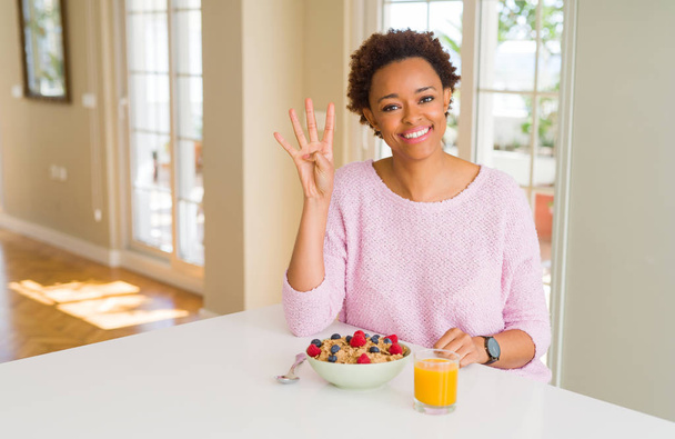 Mladá africko-americká žena, která ráno snídala doma, ukázala a ukazovala prstem číslo čtyři při úsměvu sebevědomého a šťastného. - Fotografie, Obrázek