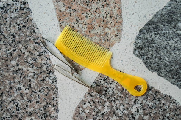 Gelber Haarkamm aus Kunststoff mit Pinzette auf Marmortisch - Foto, Bild