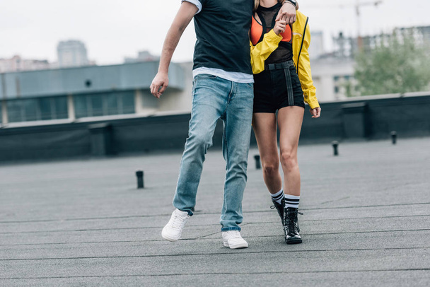 cropped view of man in t-shirt and jeans and woman in yellow jacket hugging on roof  - Fotó, kép