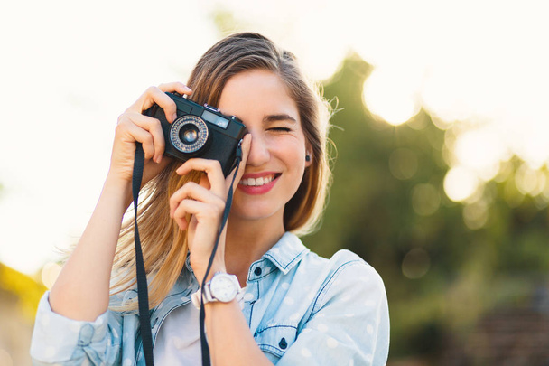 hübsches Mädchen, das an einem sonnigen Tag Fotos mit einer Vintage-Kamera macht - Foto, Bild