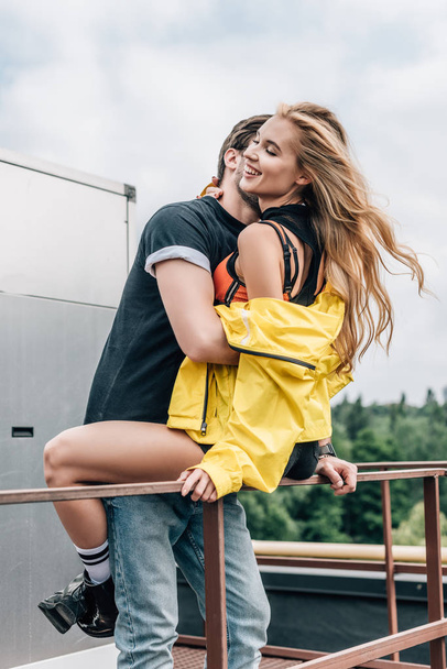 blonde woman and man in t-shirt hugging and smiling on roof  - 写真・画像
