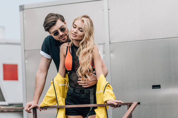 blonde woman and handsome man in glasses hugging on roof  - Photo, Image