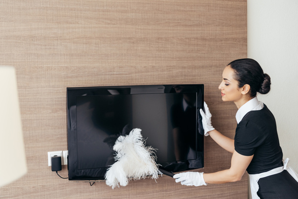 pretty maid in white gloves cleaning tv with duster - Photo, Image