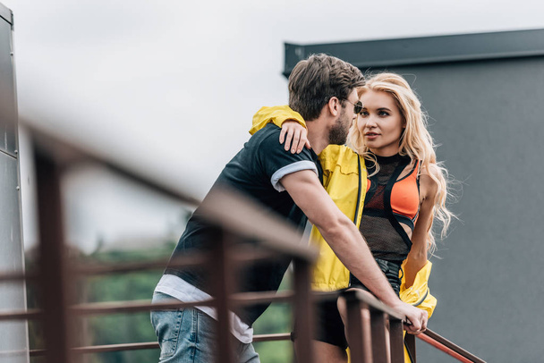 blonde woman and handsome man hugging and looking at each other on roof  - Φωτογραφία, εικόνα
