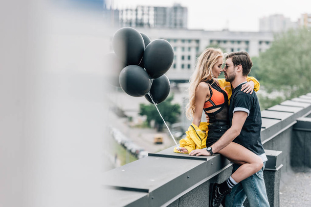 selective focus of attractive woman holding black balloons and hugging with man  - Foto, Imagen
