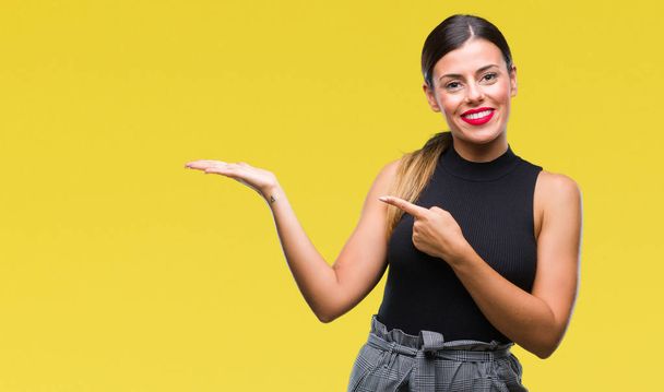 Young beautiful elegant business woman over isolated background amazed and smiling to the camera while presenting with hand and pointing with finger. - Foto, Imagen