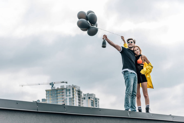 attractive woman holding black balloons and handsome man holding bottle  - Valokuva, kuva